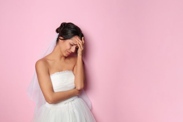 A bride in a wedding dress is standing in front of a pink wall.