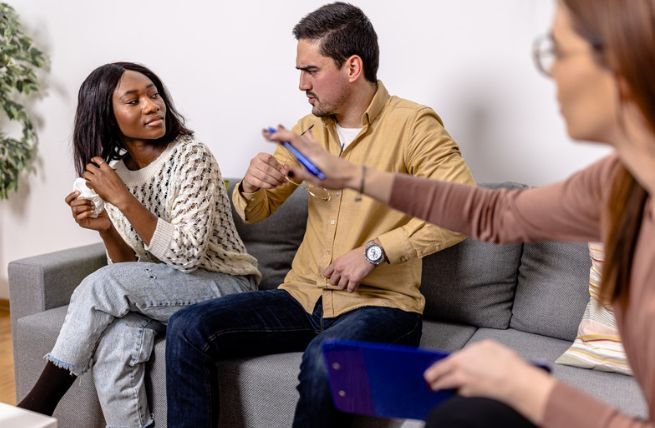 A man and a woman are sitting on a couch talking to each other.