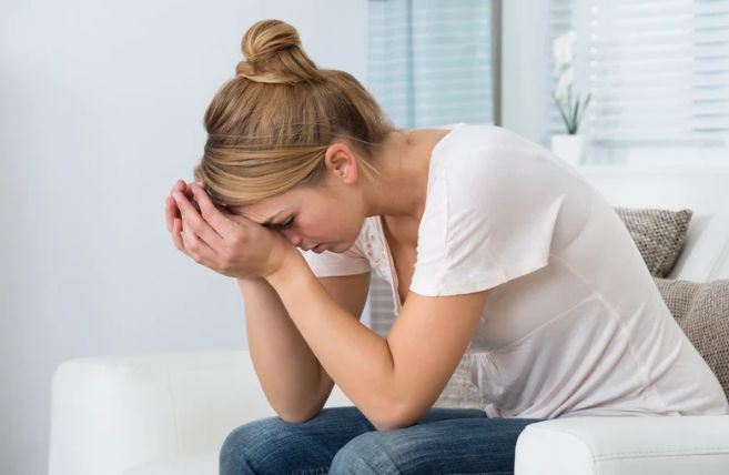 A woman is sitting on a couch with her head in her hands.