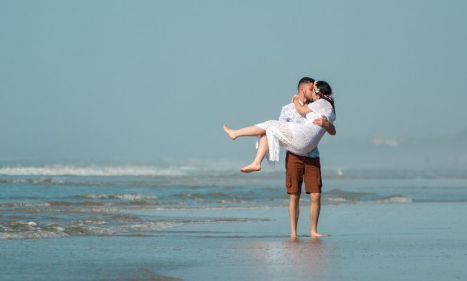 A man is holding a woman in his arms on the beach.