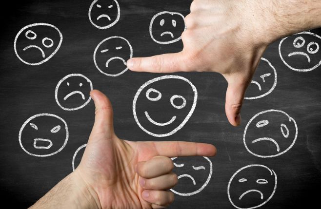 A person is pointing at a chalkboard with smiley faces drawn on it