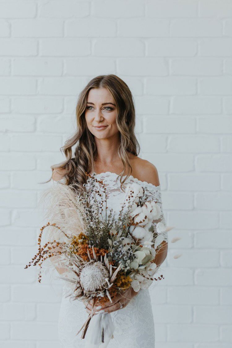 A woman in a white dress is holding a bouquet of dried flowers.