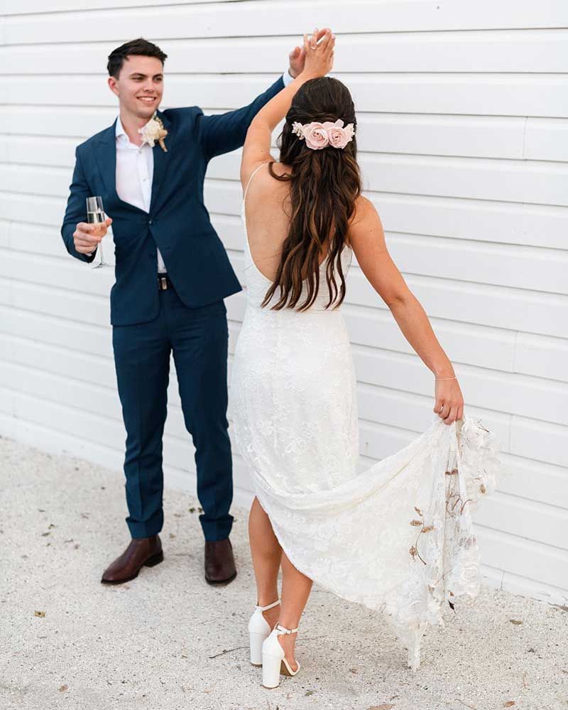 A bride and groom are dancing in front of a white wall.