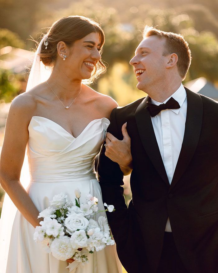 A bride and groom are standing next to each other and smiling at each other.