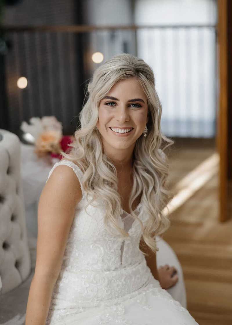 A woman in a wedding dress is sitting on a chair and smiling.