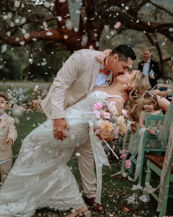 A bride and groom are kissing in front of their wedding guests.
