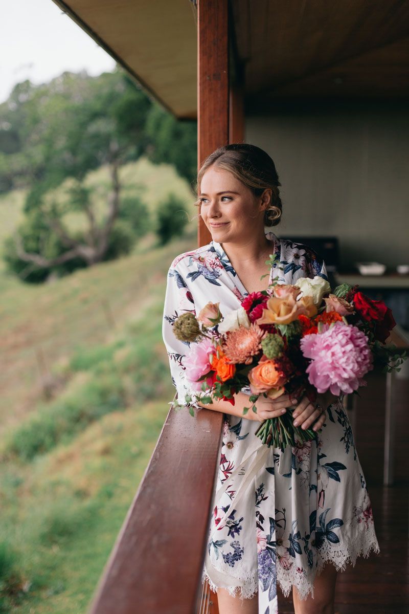A woman in a robe is holding a bouquet of flowers on a balcony.