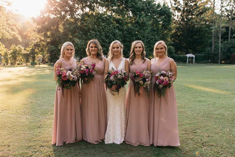 A bride and her bridesmaids are posing for a picture in a field.