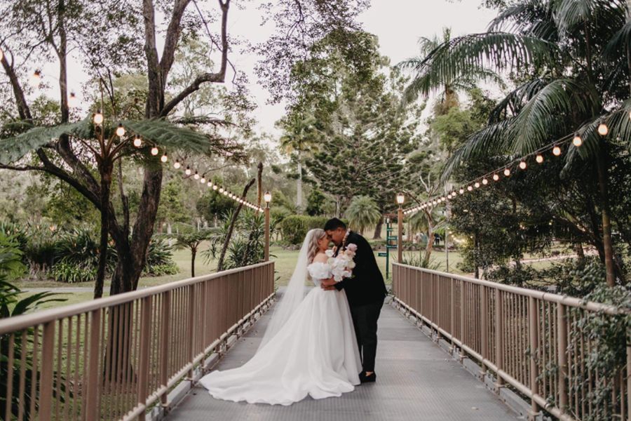 A bride and groom are kissing on a bridge.