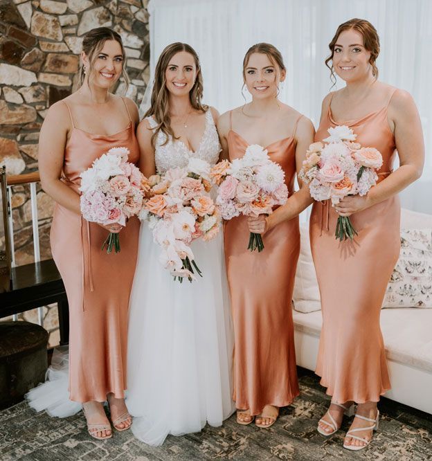 A bride and her bridesmaids are posing for a picture while holding bouquets of flowers.