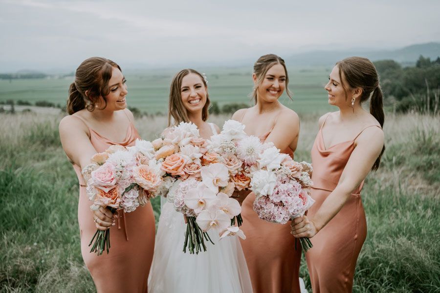 A bride and her bridesmaids are standing in a field holding bouquets of flowers.