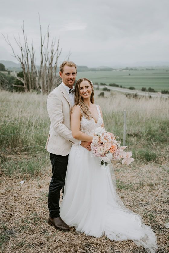 A bride and groom are posing for a picture in a field.