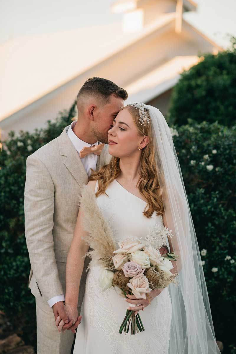 A bride and groom are kissing in front of a white building.