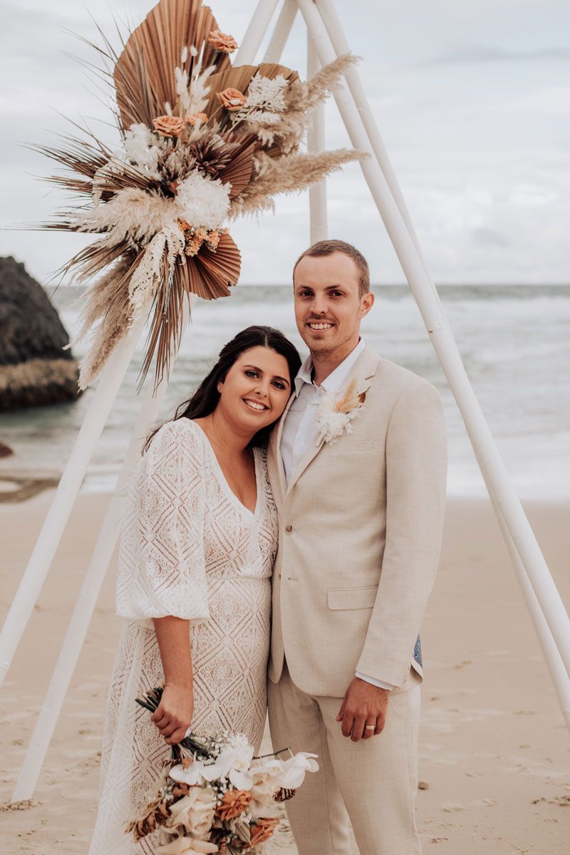 A bride and groom are posing for a picture on the beach.