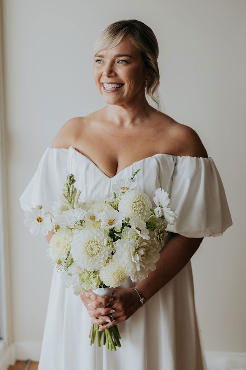 A woman in a white dress is holding a bouquet of white flowers.
