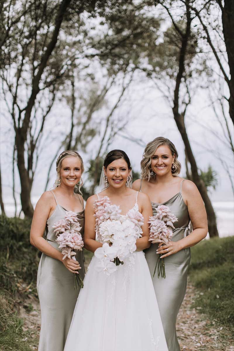 A bride and her bridesmaids are posing for a picture in the woods.