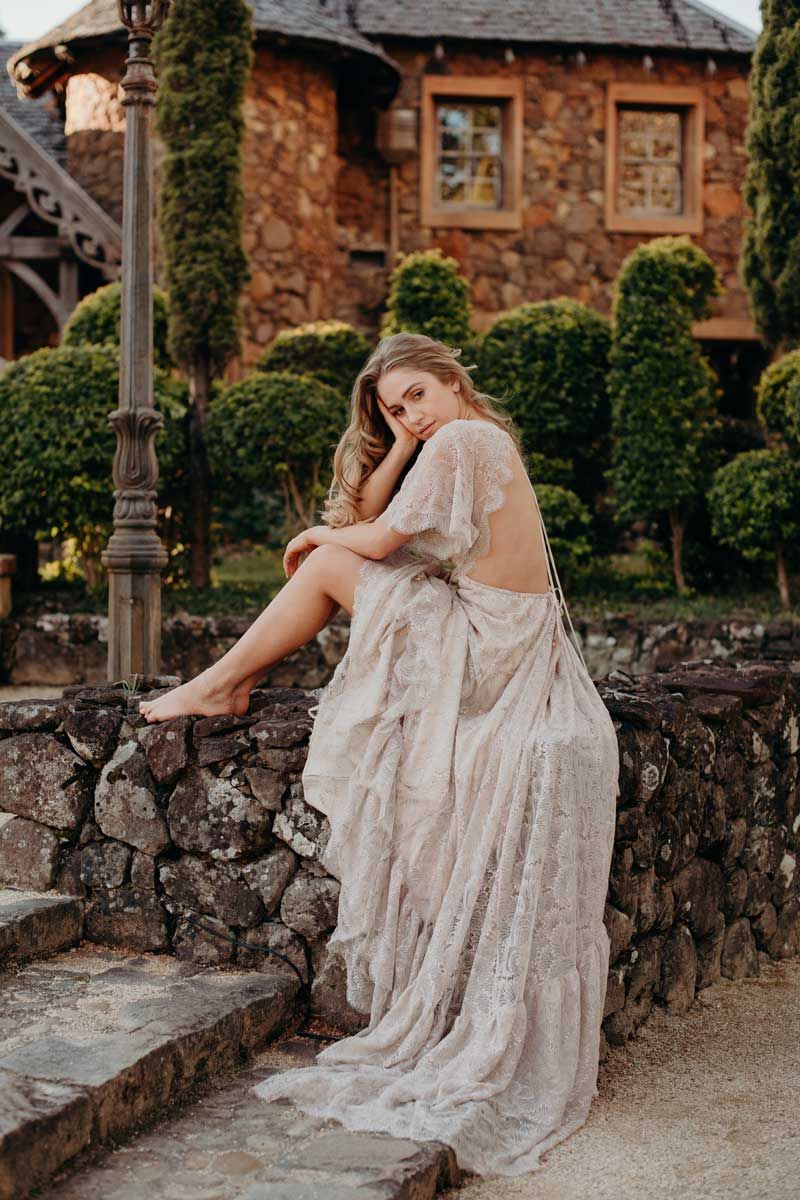 A woman in a wedding dress is sitting on a stone wall.