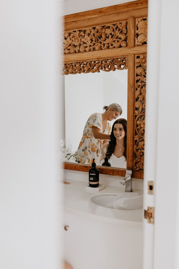 A woman is brushing another woman 's hair in a bathroom mirror.