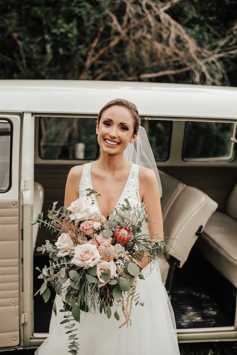 A bride in a wedding dress is holding a bouquet of flowers in front of a van.