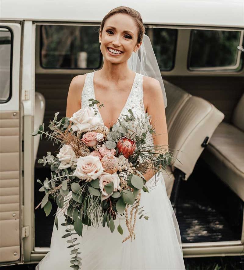 A bride in a wedding dress is holding a bouquet of flowers in front of a van.