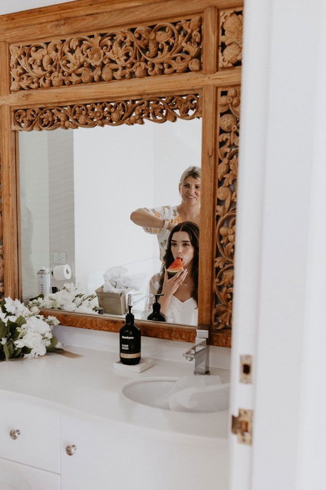 A woman is getting her hair done in a bathroom mirror.
