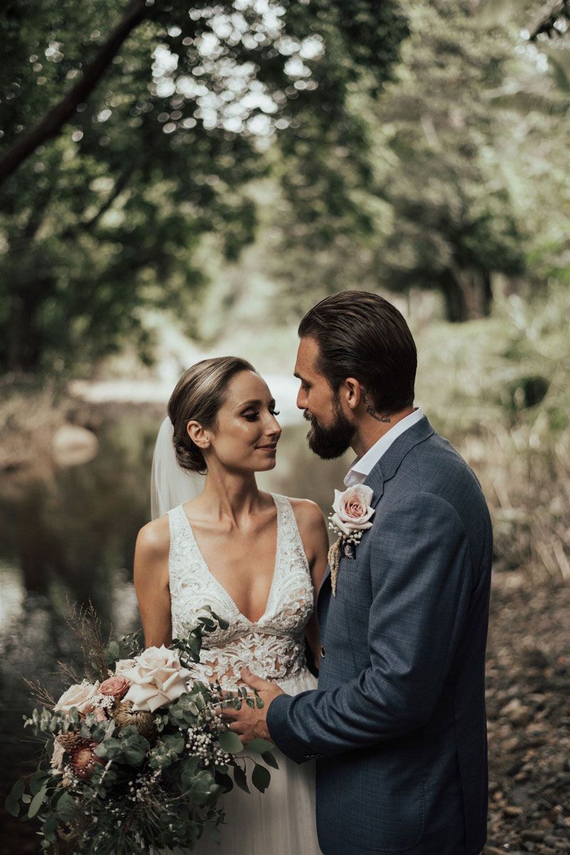 A bride and groom are standing next to each other in front of a river.