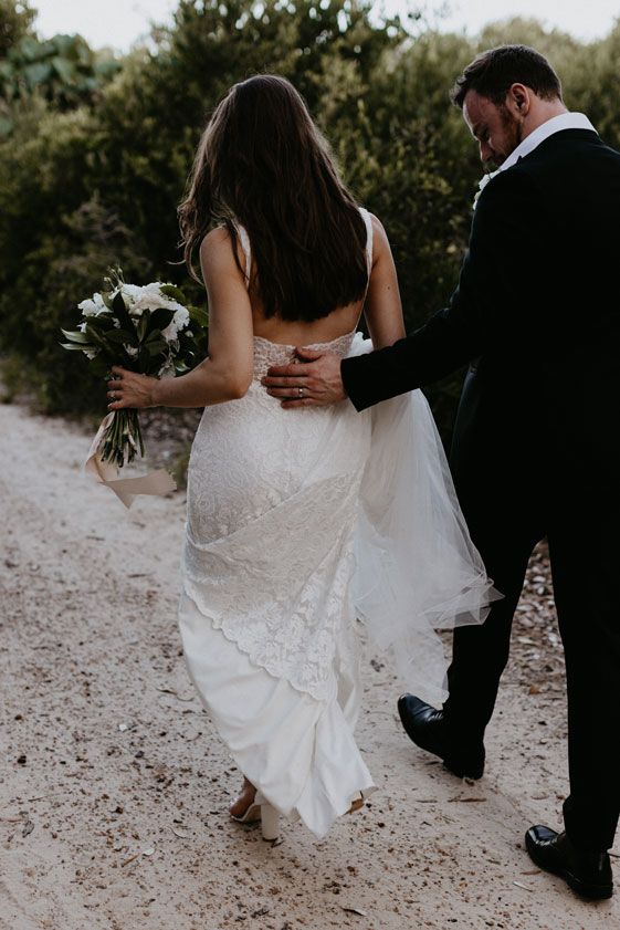 A bride and groom are walking down a dirt road.