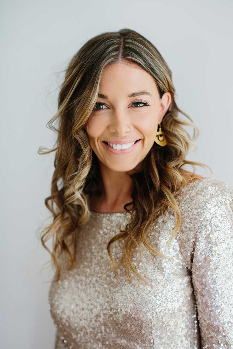 A woman wearing a sequined top and earrings is smiling for the camera.
