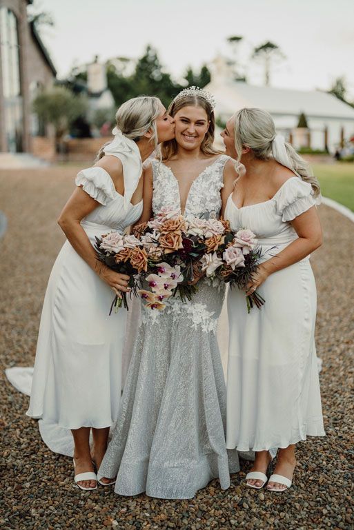 The bride and her bridesmaids are kissing the bride on the cheek.