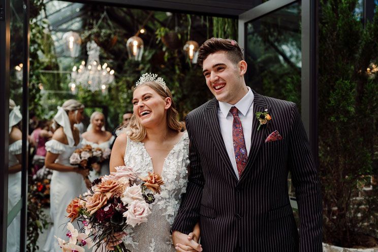 A bride and groom are walking down the aisle at their wedding holding hands and smiling.