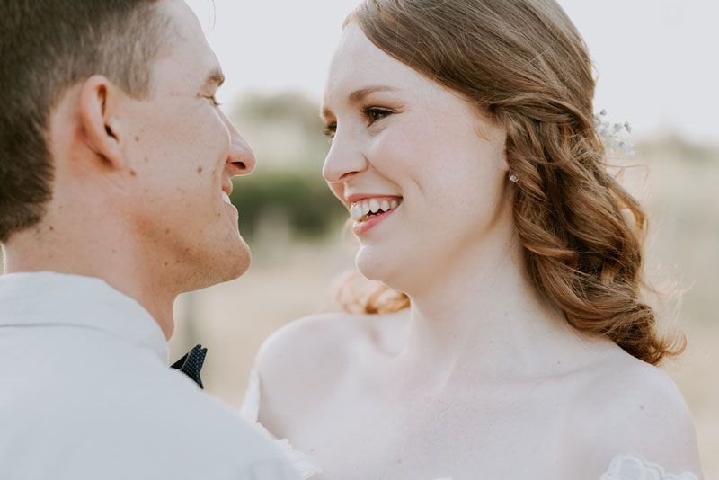 A bride and groom are looking at each other and smiling.