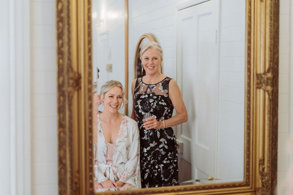 Two women are standing next to each other in front of a mirror.