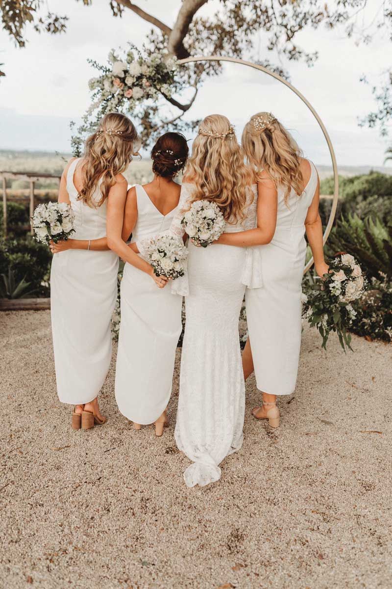 A bride and her bridesmaids are standing next to each other in front of a tree.