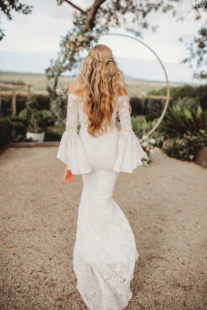 A woman in a white dress is walking down a gravel road.