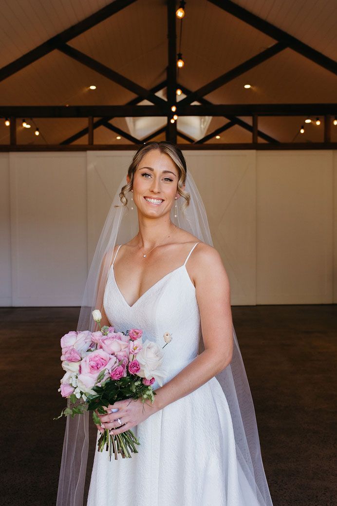A bride in a white dress and veil is holding a bouquet of pink flowers.