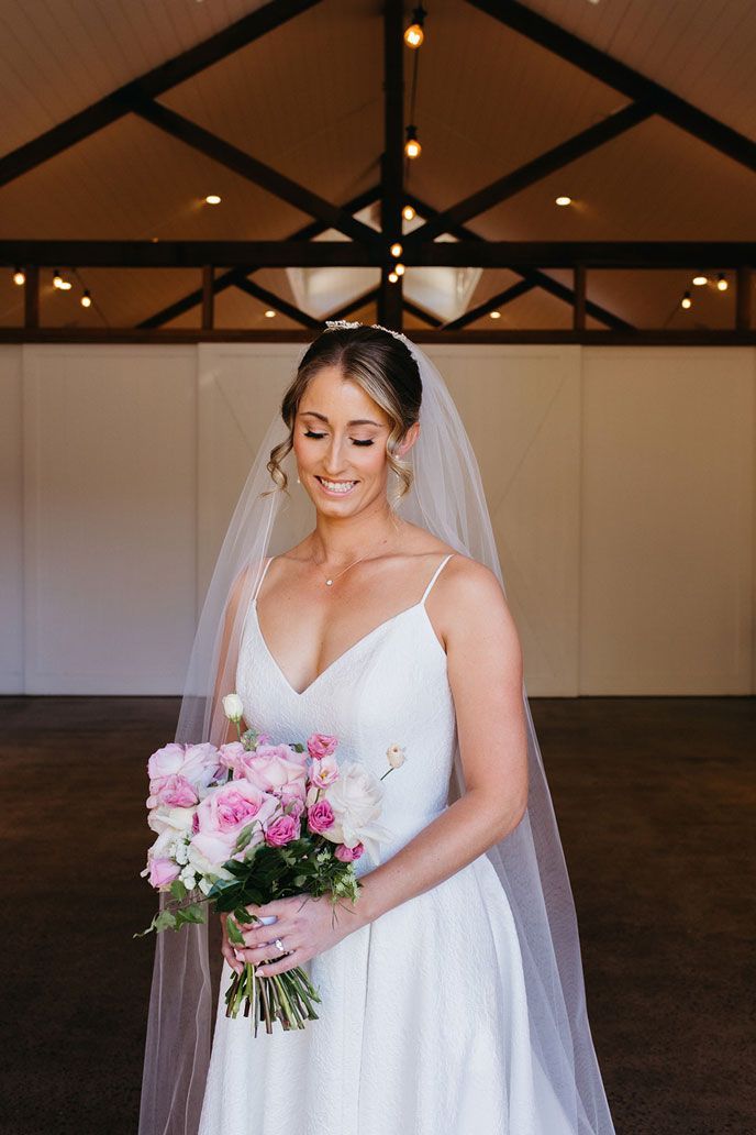 A bride in a white dress and veil is holding a bouquet of pink flowers.