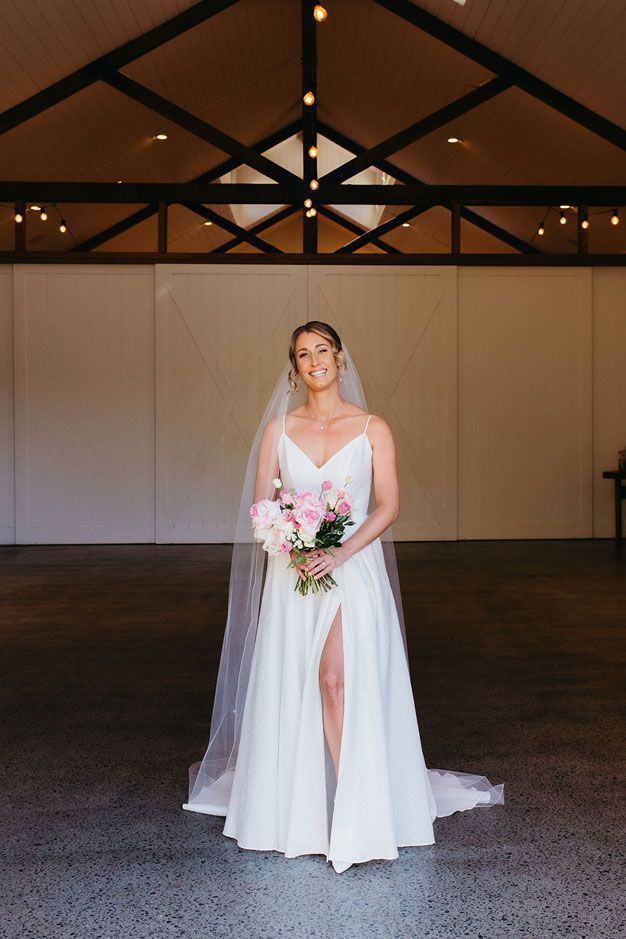 A bride in a white dress and veil is standing in a room holding a bouquet of flowers.