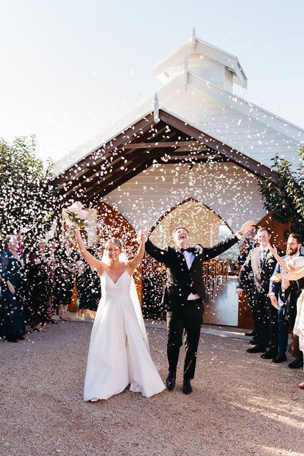 A bride and groom are standing in front of a church surrounded by confetti.