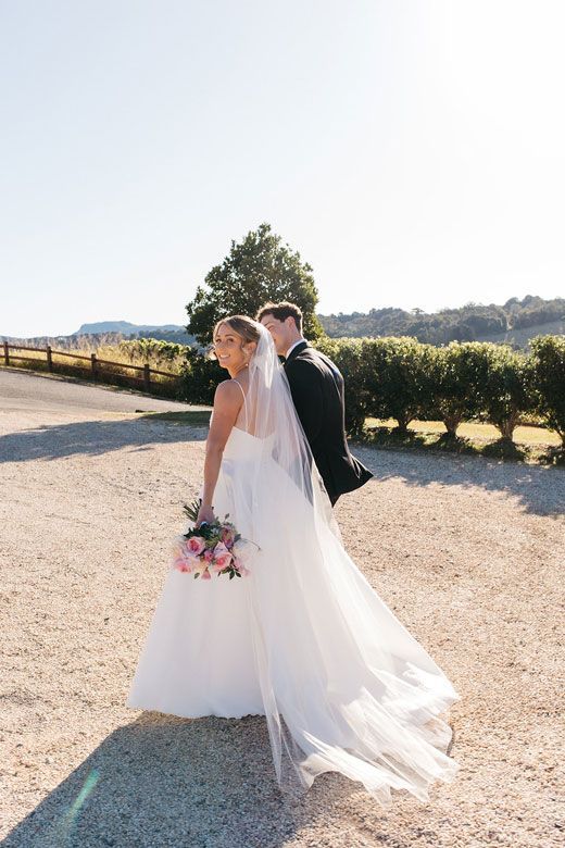 A bride and groom are walking down a dirt road.