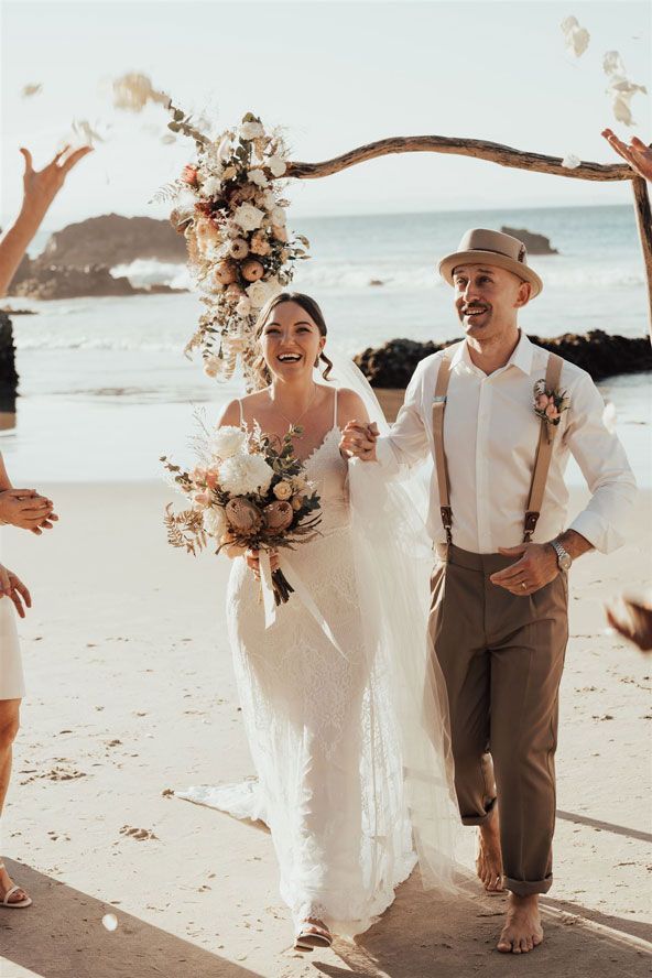 A bride and groom are walking down the beach after their wedding ceremony.