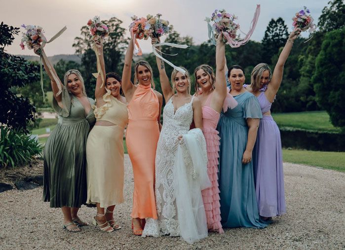 A bride and her bridesmaids are posing for a picture with their arms in the air.