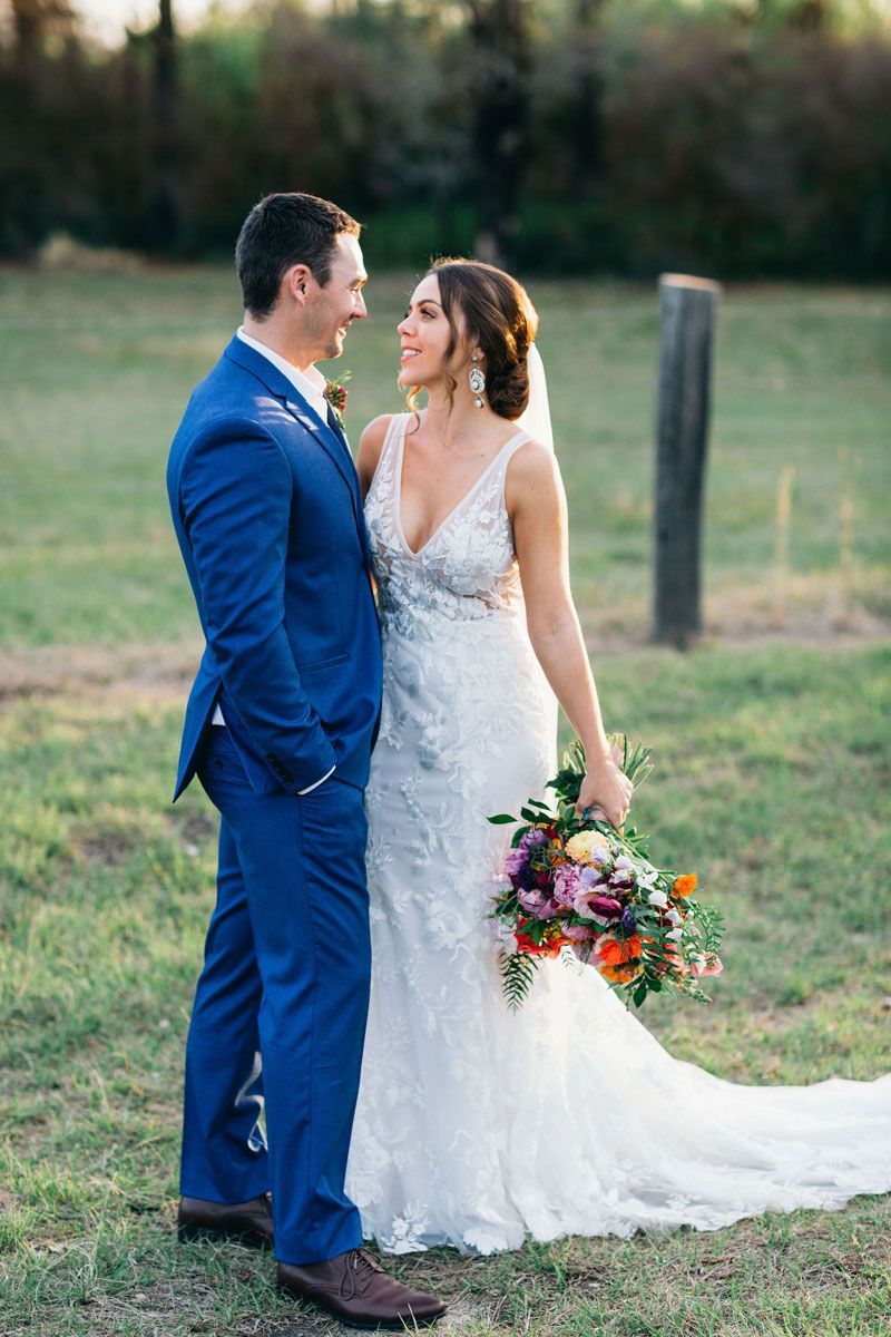 A bride and groom are standing next to each other in a field.