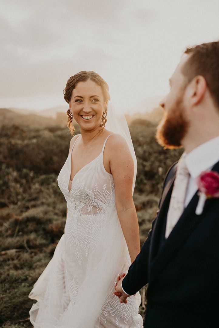 A bride and groom are holding hands and walking in a field.