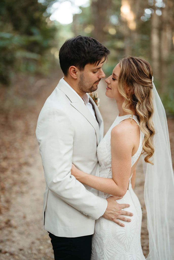A bride and groom are standing next to each other in the woods.