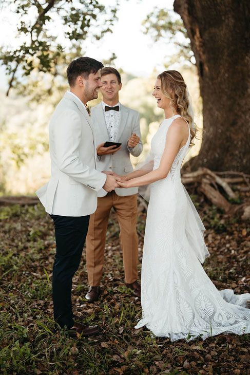 A bride and groom are holding hands during their wedding ceremony under a tree.