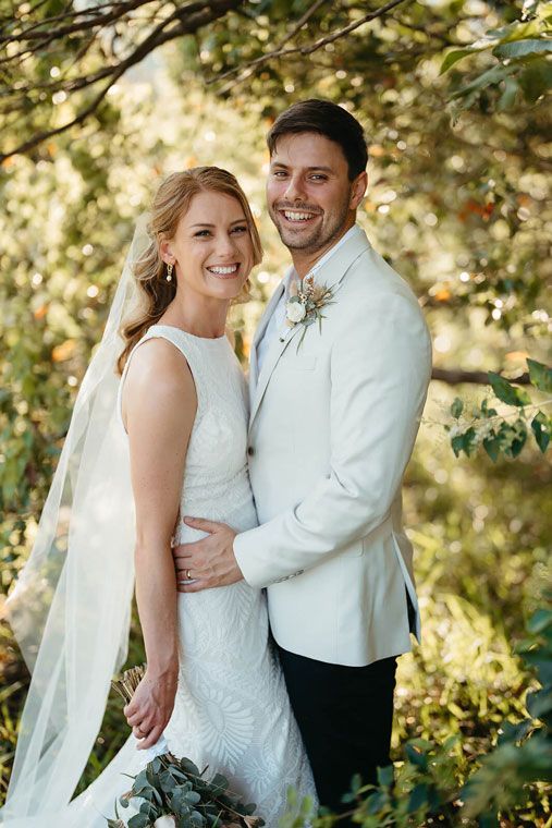 A bride and groom are posing for a picture in the woods.