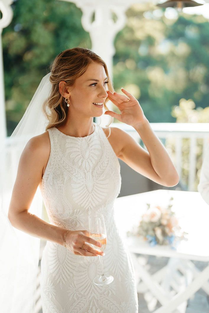The bride is wearing a white dress and holding a glass of wine.