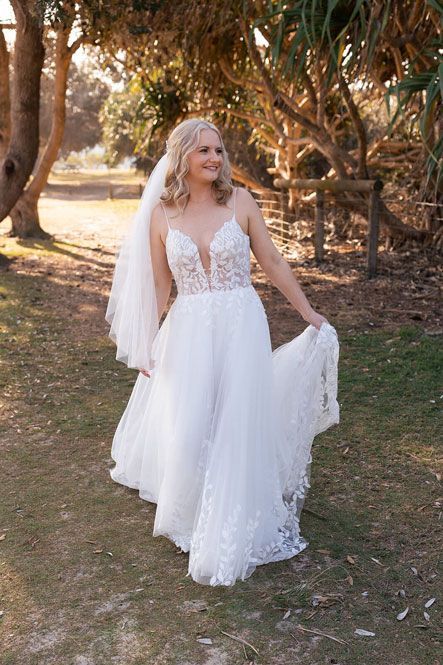 A woman in a wedding dress and veil is standing in a field.
