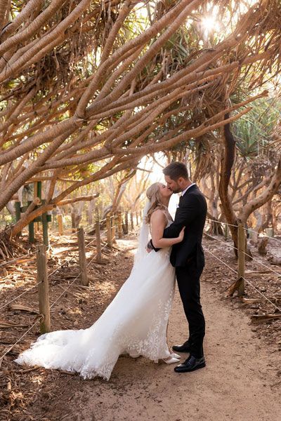 A bride and groom are kissing under a canopy of trees.