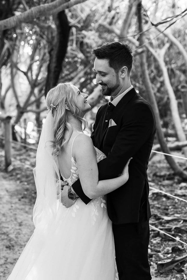 A black and white photo of a bride and groom hugging in the woods.